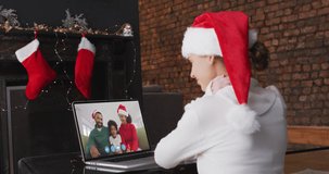 Animation of snow falling over caucasian girl in santa hat on laptop video call at christmas. christmas, tradition and celebration concept digitally generated video.