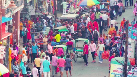 Haridwar, Uttarakhand, India - circa 2021: aerial high angle shot of crowd of people on a busy street with a market bazaar on the side, rickshawas and two wheelers moving around and some people