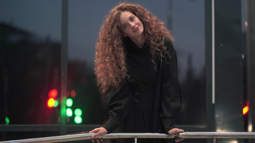A beautiful Caucasian woman with curly hair, standing near a mirrored building, and waving her hair in different directions. High quality 4k footage