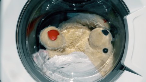 Teddy Bear rolling inside of washing machine during laundry. Plush toy in the washing machine. Cleaning the child's toys.