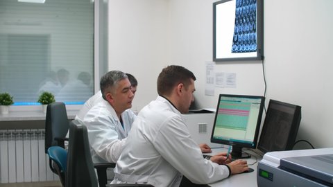 Three male doctors use a computer during a consultation at a medical hospital.