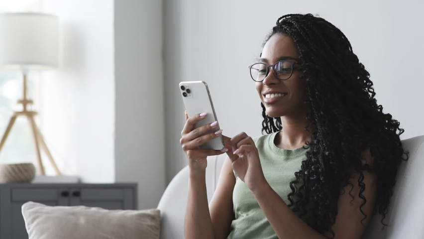 Young woman using smartphone at home. African american girl looking at mobile phone in her room. Communication, work or study from home, connection, mobile apps, technology, lifestyle concept | Shutterstock HD Video #1080824372