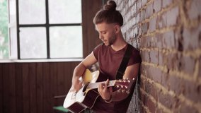 Man with acoustic guitar leaning against brick wall playing music singing songs enjoy life Handsome caucasian male guitar player practice play musical instrument home loft interior Creative lifestyle  - Powered by Shutterstock - Get 15% off with code: PIKWIZARD15