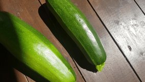 4k video, two whole zucchini on a dark wooden background, sunlight on a summer day