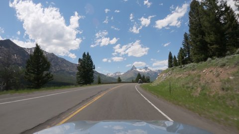 POV Driving a car on asphalt road in Montana mountains leading to Yellowstone National Park. Blue sky on sunny day	