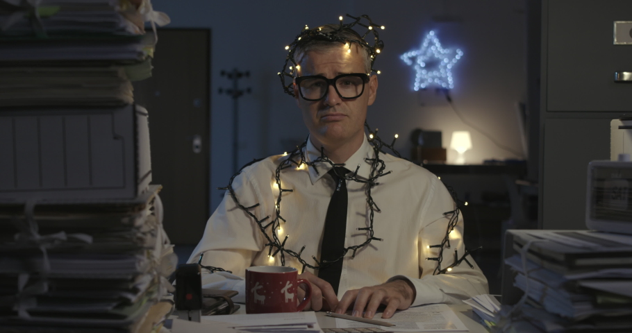 Sad corporate businessman working on Christmas day, he is wrapped in Christmas lights | Shutterstock HD Video #1080833333