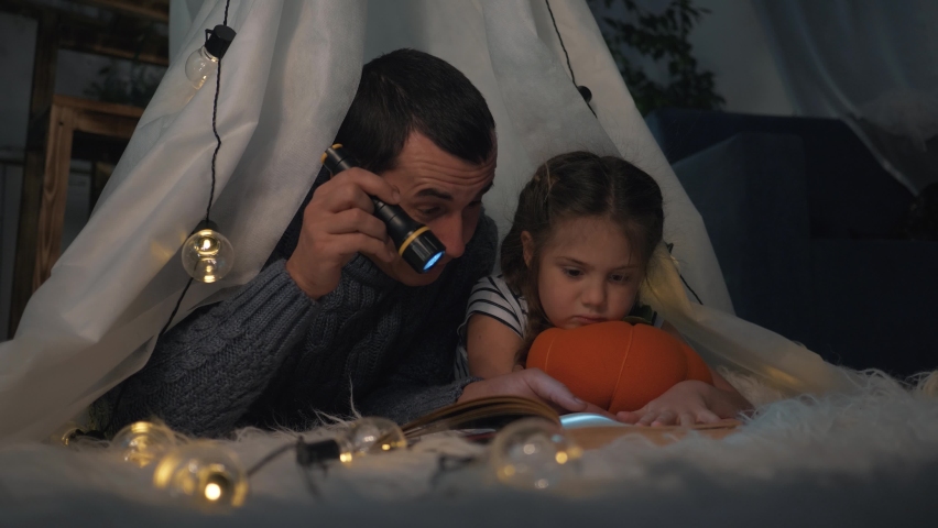 Happy family. Father and daughter in tent reading book with lantern. Happy family game. Daughter and father are reading book in tent. Child dream in tent with lantern. Happy family dream and play | Shutterstock HD Video #1080836324