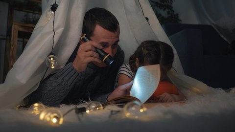 Happy family. Father and daughter in tent reading book with lantern. Happy family game. Daughter and father are reading book in tent. Child dream in tent with lantern. Happy family dream and play