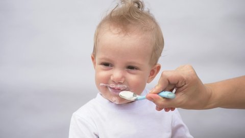 mother feeds her little son from a spoon with porridge. The kid is eating breakfast from a spoon. loving mother takes care of the child, spoon feeds porridge. Handsome smiling cute kid. Children food