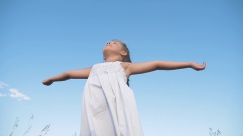 Happy child on background sky.girl stands with raised arms in sunny blue sky outdoors.child enjoys freedom, happiness, raising his hands up.girl of freedom, happiness, enjoying nature while traveling.