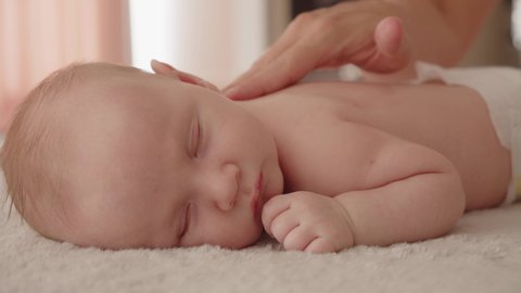 Masseuse pours massage oil on the baby's body and does a massage. Small Caucasian newborn lies on his stomach while a masseuse massages his small back and develops muscles. Beauty treatments child .