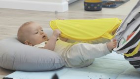 Baby lying on the floor playing with toy storage basket, cute 7 month old baby boy having fun exploring new world around him at home. High quality 4k footage