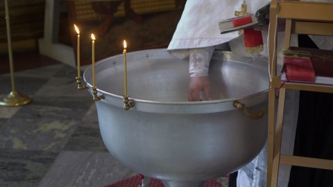 Priest touching and mixing water with hand before the baptism ceremony. Font for christening in the Orthodox Church. Religion - Christianity or Catholicism.