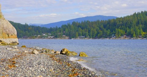 Establishing shot of ocean beach with rocks and pebbles in slow motion at summer day in Vancouver, Canada, North America. Day time on September 2021. Still camera. ProRes 422 HQ.