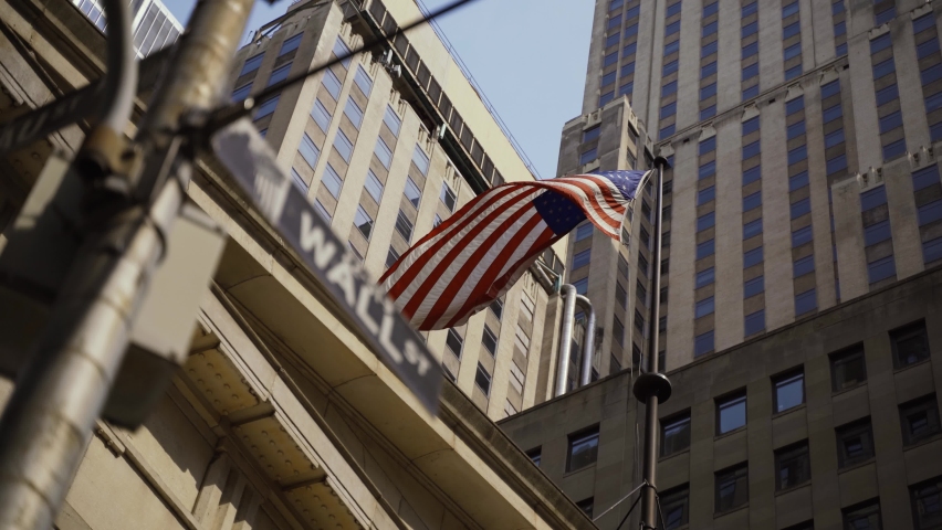 Wall Street sign with American flags in the background, shot in the heart of the business world in Manhattan. Business, finance, worldwide stock trade and economics concept. Royalty-Free Stock Footage #1080844415