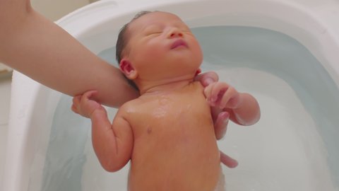Calm of asian newborn baby bathing in bathtub.mother bathing her son in warm water.7 days of adorable newborn infant smile in tub relax and comfortable.Newborn baby care concept