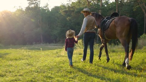 A cowboy with a horse and his beautiful daughter are walking in the pasture. Happy cowboy family. Slow motion.