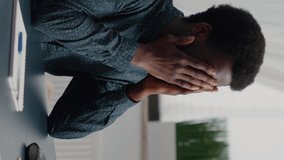 Vertical video: Stressing african american man with big headache pain, suffering from migraine, rubbing his temples. Overwhelmed manager working from home office, exhausted guy from problems and job