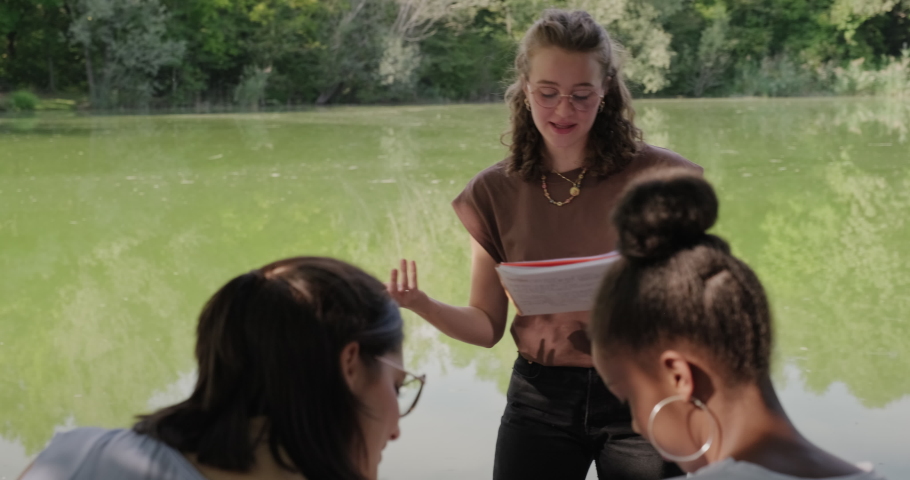 Young women at school, group of four girls talking and studying for college test near lake in city park. Teens and education with happy white and black students reviewing assignment | Shutterstock HD Video #1080861629