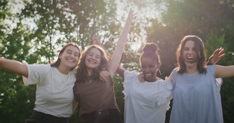 Youth culture with happy young people, group of female friends in park. Multiethnic teens outdoors, women smiling and laughing. Portrait of teenagers together, girls looking at camera. Slow motion