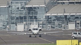 A small plane rides in the background of the airport building. Slow motion video of a private plane traveling to disembark passengers