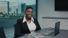 Portrait Of Smiling Black Businesswoman Posing At Workplace In Modern Office, Confident African American Female Entrepreneur In Formal Wear Sitting At Desk And Looking At Camera, Slow Motion Footage