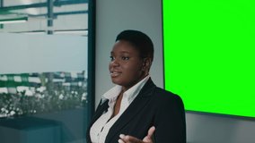 Confident Black Businesswoman Making Presentation In Office, Standing Near Green Chroma Key Screen, African American Female Entrepreneur Giving Speech During Conference In Boardroom, Slow Motion