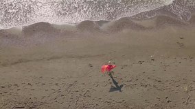 Drone view of the beautiful waves on a sandy beach, a woman enters the sea in a red stole, and dances, she is happy, the sea waves break on the sandy coastline.