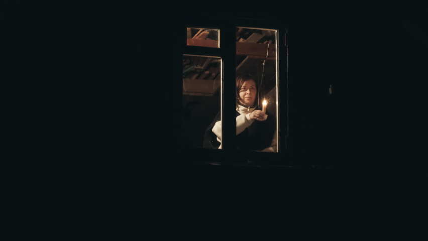 Woman in a cowboy hat in the attic of a house. She gives a signal with a candle from the window. The concept of old, retro films about conspiracies, intrigues Royalty-Free Stock Footage #1080875513
