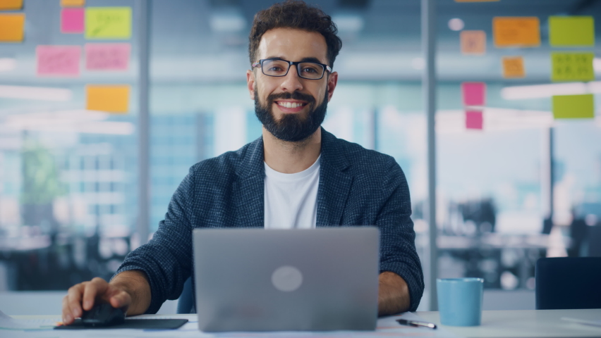 Modern Office: Portrait of Stylish Hispanic Businessman Works on Laptop, Does Data Analysis and Creative Designer, Looks at Camera and Smiles. Digital Entrepreneur Works on e-Commerce Startup Project Royalty-Free Stock Footage #1080878453