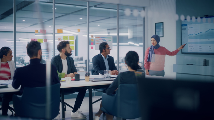 Multi-Ethnic Office Conference Room. Muslim Female CEO Wearing Hijab does Presentation for Group of Managers Talk, Use TV Infographics, Statistics. Businesspeople Brainstorm eCommerce Growth Strategy Royalty-Free Stock Footage #1080878555