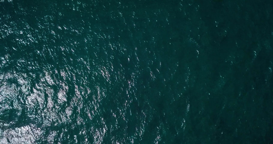 Overhead shot drone of The The sea surface with calm waves and looks sparkling reflecting the sun. The sea water looks bluish. Watu Kodok Beach, Indonesia. Royalty-Free Stock Footage #1080880187