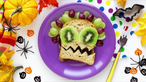 Stop motion animation of Fun Food for kids preparation process of cute Halloween monster sandwich with chocolate spread and fresh grapes and kiwi fruit