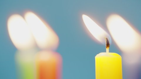 Close up of colorful birthday candels light up with a match isolated on blue background shot in 4k super slow motion
