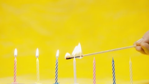 Colorful birthday candels light up with a match isolated on yellow background shot in 4k super slow motion