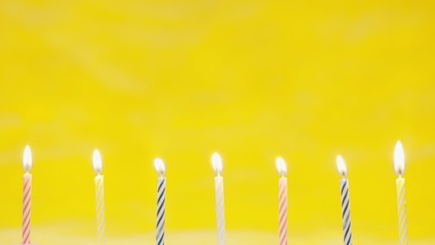 Blow off colorful birthday candels isolated on yellow background shot in 4k super slow motion