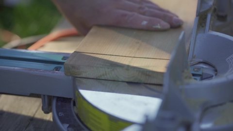 Man's hands separating sawed off wooden piece from mitre saw. Slow motion