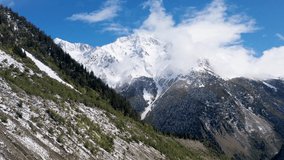 Aerial view of snow-capped mountains, rocks, gorge, trees. The mountains are hidden behind the clouds. Snowy mountain peak, clouds in the sky. Glacier on the mountain. 4K drone video.