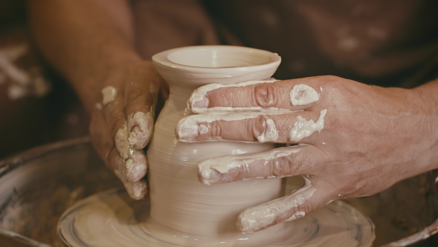 Male Potter Shaping Clay Into A Ceramic Mug Working On Pottery Wheel Indoors, Closeup Of Muddy Hands. Craft Making Hobby And Creative Profession Concept. Cropped Shot