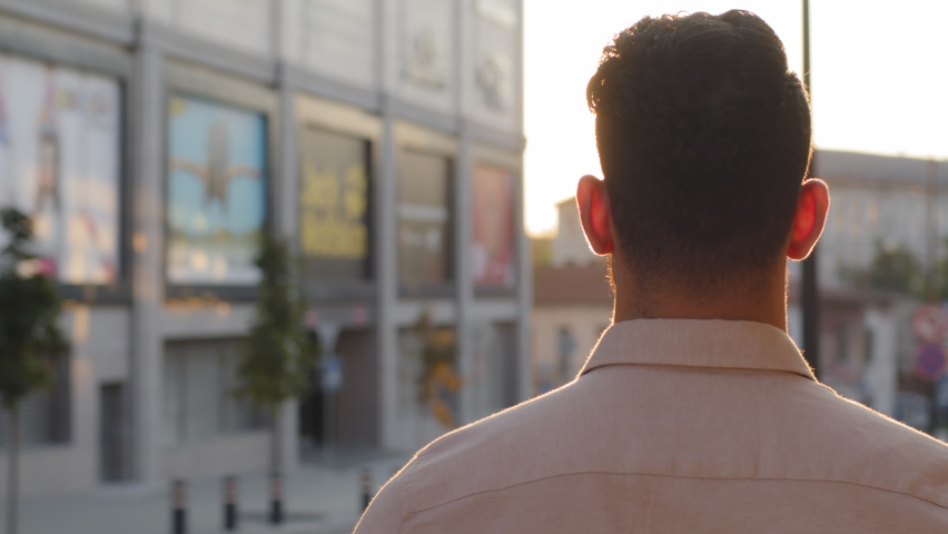 View from behind unrecognizable brunette man back view businessman guy in formal shirt tourist standing in city outdoors looking at urban buildings enjoying sunset sunlight male silhouette in sun rays | Shutterstock HD Video #1080888599
