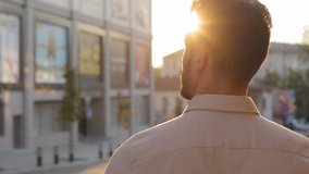 View from behind unrecognizable brunette man back view businessman guy in formal shirt tourist standing in city outdoors looking at urban buildings enjoying sunset sunlight male silhouette in sun rays