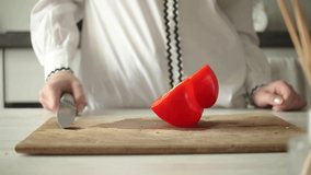 Slicing red bell pepper on wooden cutting board by chef. Female hands is cutting the paprika vegetables. Health eating and diet food concept video