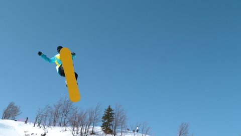 SLOW MOTION TIME WARP: Athletic male tourist snowboarding in Japanese mountains jumps into the air and performs a spinning grab trick. Spectacular shot of a young male snowboarder catching big air.