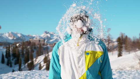 SLOW MOTION TIME WARP, CLOSE UP, DOF: Stoked male snowboarder gets hit in the head by a large wet snowball. Cinematic shot of a happy young male tourist wearing goggles getting hit by a snowball.