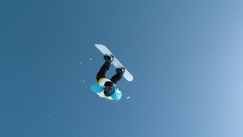 SLOW MOTION: Unrecognizable snowboarder jumps off a kicker and does an acrobatic flip trick. Male tourist snowboarding in Slovenia does a spectacular backflip. Shot of a snowboarder doing tricks.