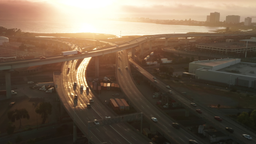 Cinematic golden sunset light glowing and reflecting from scenic 4K highway. Aerial view busy road with bay on background. Vehicles driving in different directions by freeway and rams on summer day Royalty-Free Stock Footage #1080893822