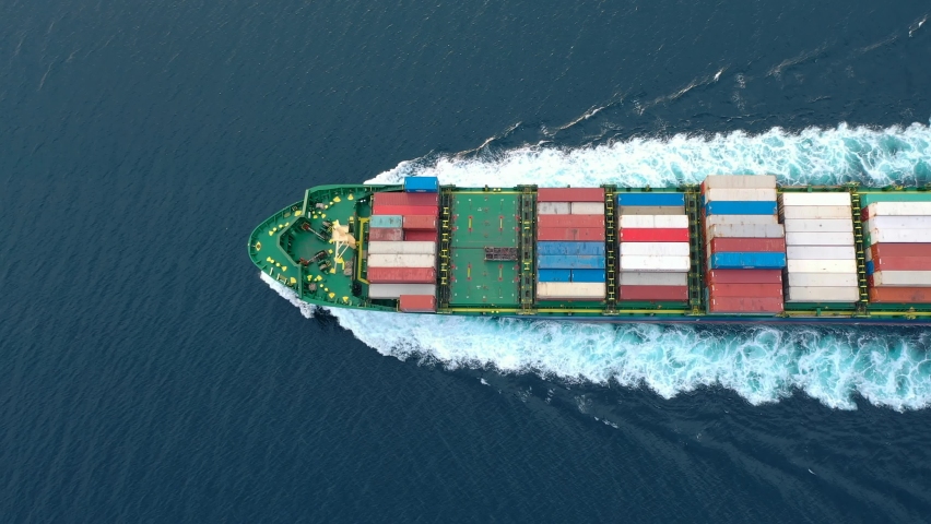 Container Ship ploughs through calm waters. Topmost complete deck extends from bow to aft. Nice deep green shade of ocean, white trail after large powerful vessel. Aerial, birds eye view
 Royalty-Free Stock Footage #1080902249