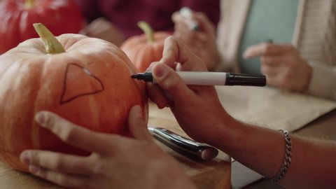 A man draws on a pumpkin with a marker and carefully examines the lamp
