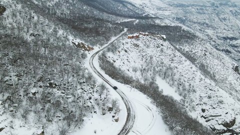 Aerial flight in winter landscape. Black car driving along winter covered snowy road between mountains. Caucasus mountain travel, Armenia. Drone views.