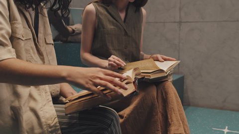 Midsection slowmo shot of two unrecognizable female university students sitting on stairs turning book pages while studying